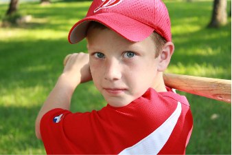 Мальчик в спортивной майке и бейсболке с бейсбольной битой на зелёном газоне (сайт Минской школы киноискусства)